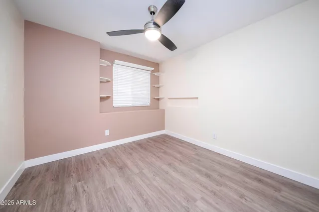 an empty room with wooden floor ceiling fan and windows