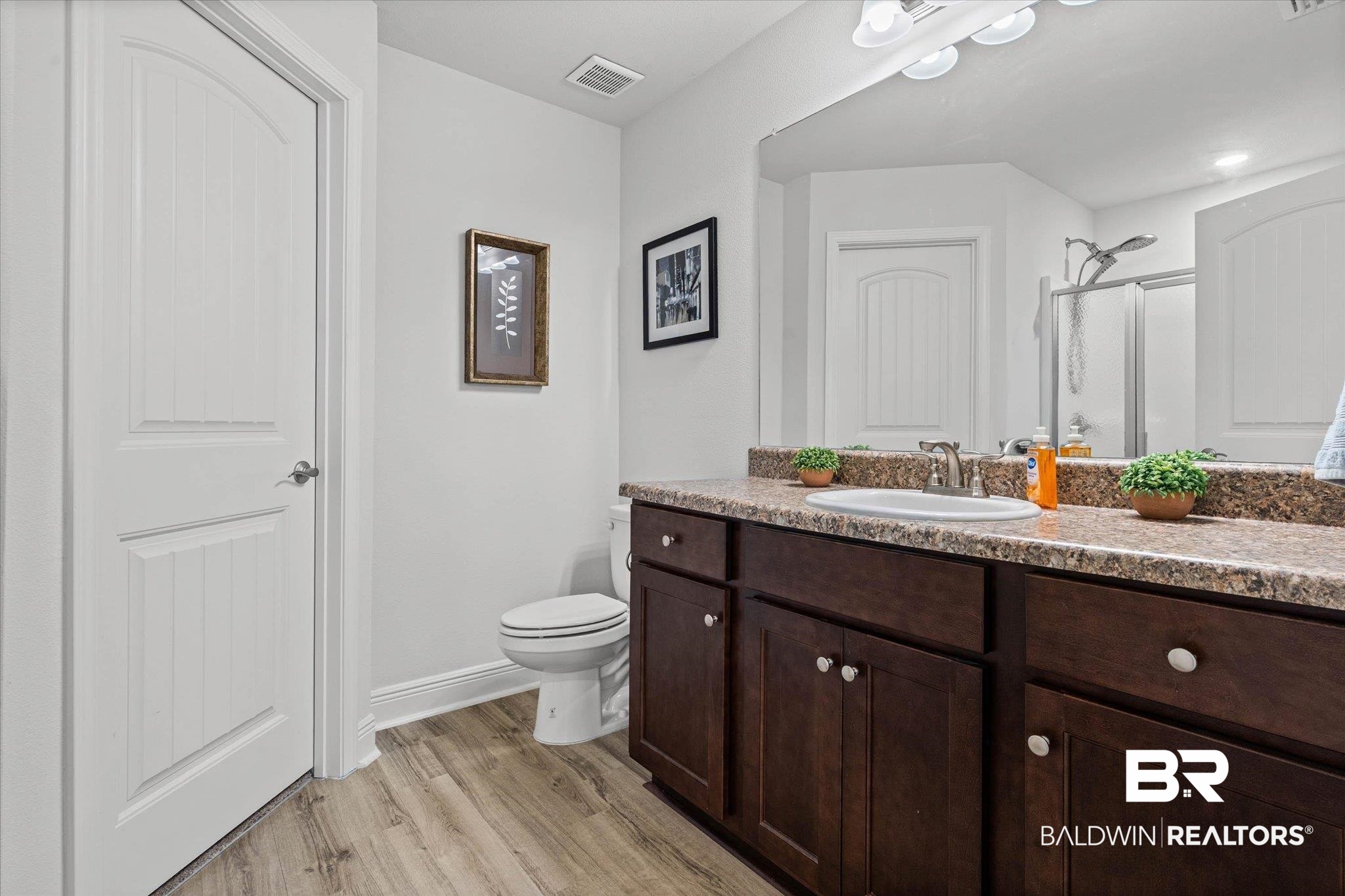 22420 Respite Lane Foley, AL 36535 - Photo 12 of 35 Bathroom featuring a wood-finish floor, a dark wood vanity with white knobs, a built-in sink, and a speckled countertop