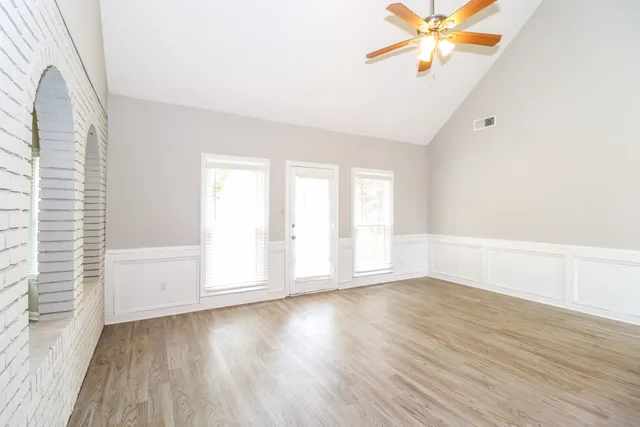 an empty room with wooden floor fan and windows