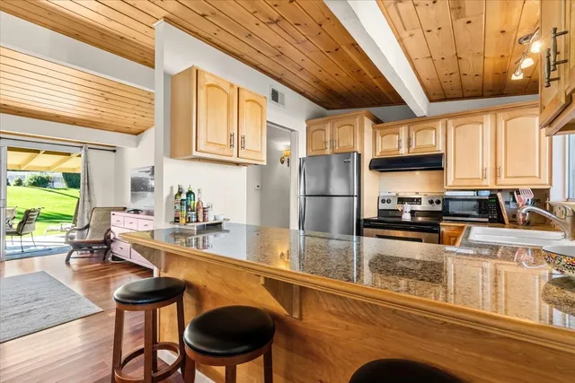 a kitchen with stainless steel appliances granite countertop a stove a refrigerator a sink a dining table and chairs with wooden floor