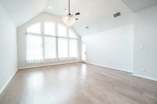 an empty room with wooden floor and windows with curtains