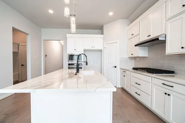 a kitchen with stainless steel appliances a stove a sink a refrigerator and white cabinets with wooden floor