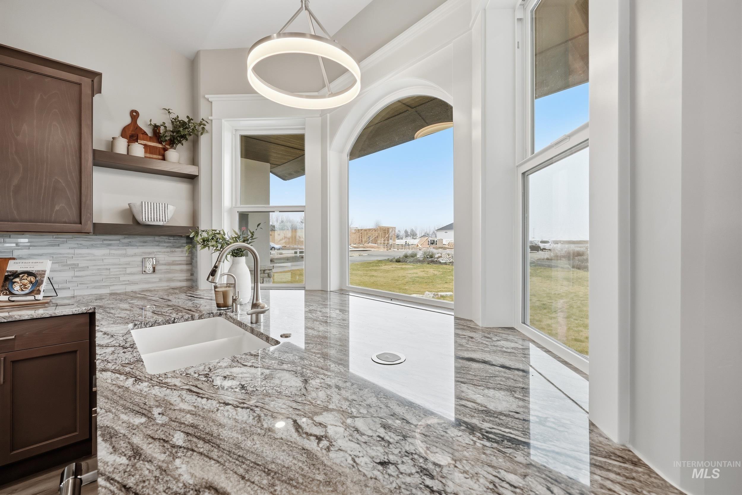 9264 Basin Kid Court Middleton, ID 83644 - Photo 11 of 50 Kitchen featuring light stone counters, plenty of natural light, tasteful backsplash, and dark brown cabinetry