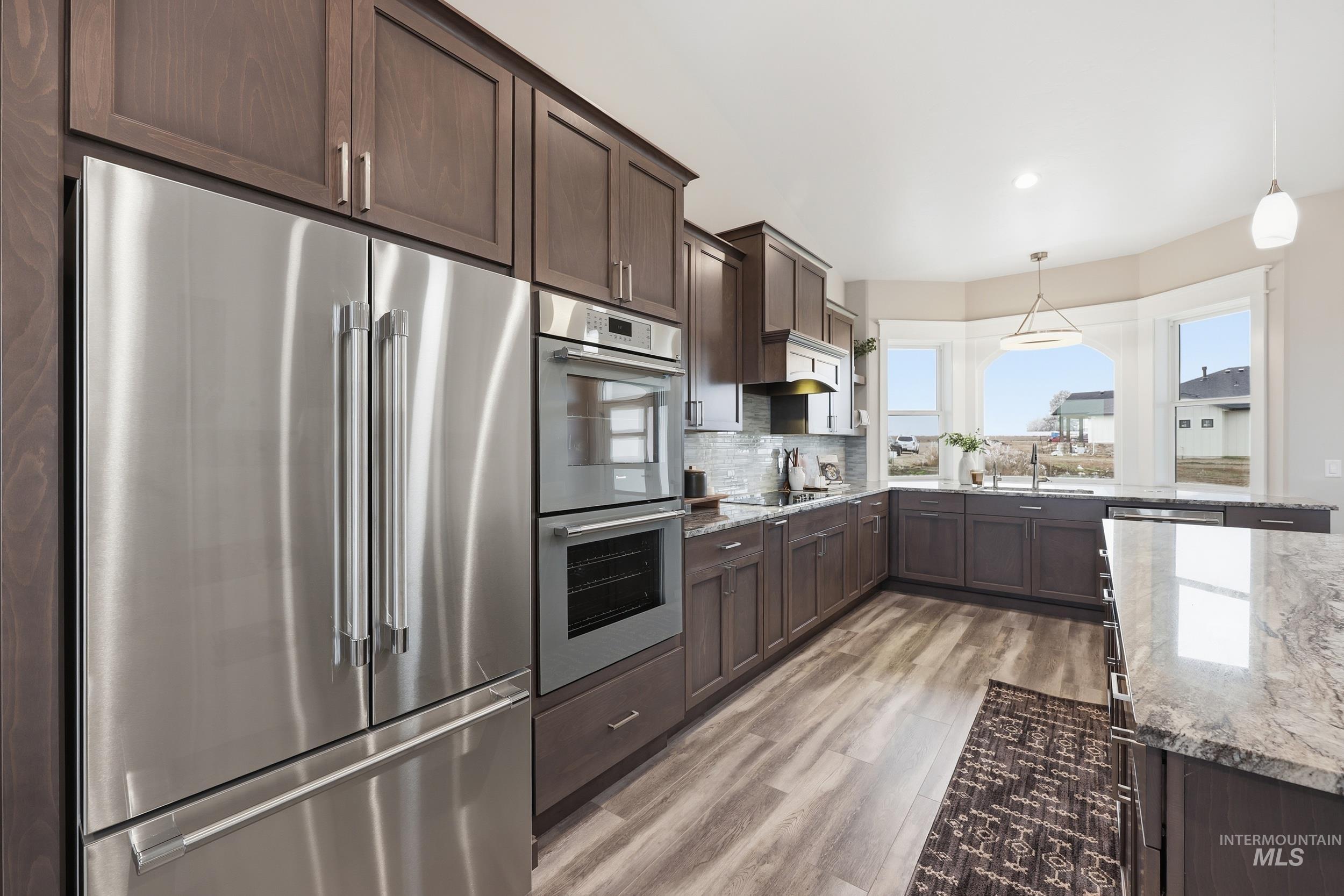 9264 Basin Kid Court Middleton, ID 83644 - Photo 13 of 50 Kitchen with stainless steel appliances, dark brown cabinets, light stone counters, hanging light fixtures, and recessed lighting