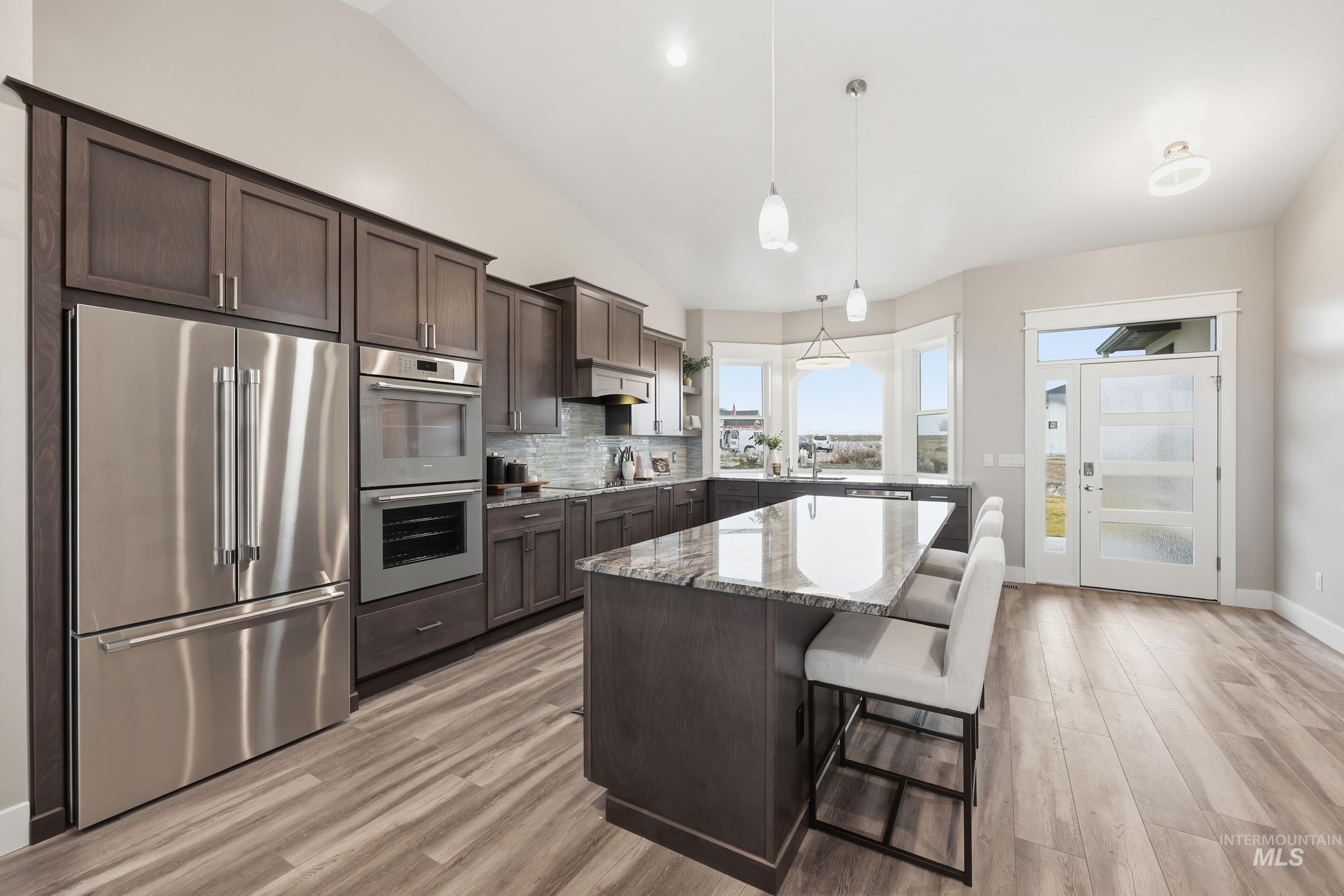 9264 Basin Kid Court Middleton, ID 83644 - Photo 5 of 50 Kitchen with appliances with stainless steel finishes, dark brown cabinets, light stone counters, a kitchen breakfast bar, and decorative light fixtures