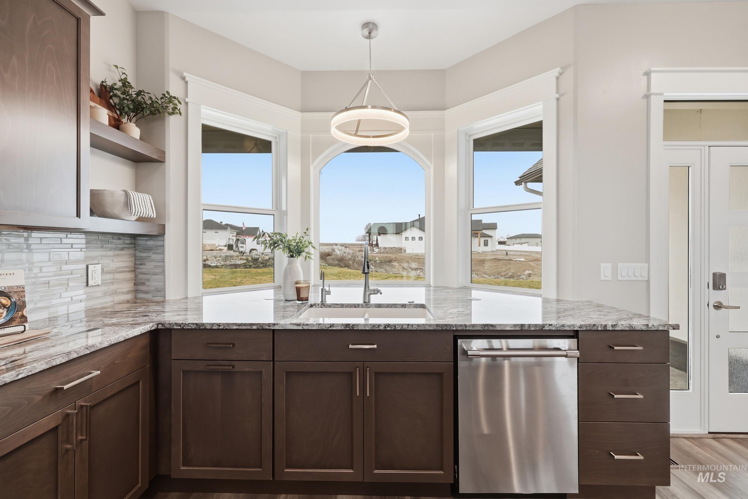 9264 Basin Kid Court Middleton, ID 83644 - Photo 10 of 50 Kitchen with dark brown cabinetry, dishwasher, light stone countertops, and hanging light fixtures