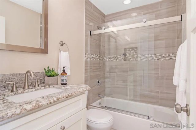 a bathroom with a granite countertop bathtub shower sink vanity and toilet
