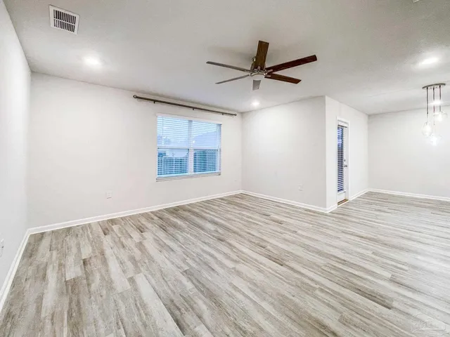 an empty room with wooden floor fan and windows