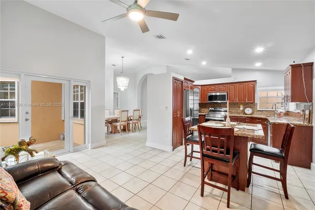 a room with stainless steel appliances kitchen island granite countertop a dining table chairs and a refrigerator