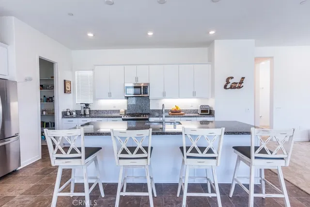 a kitchen with stainless steel appliances kitchen island granite countertop a dining table chairs refrigerator and sink