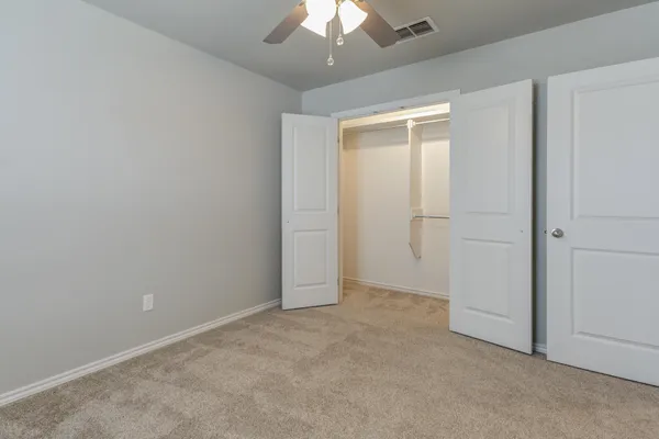 an empty room with a chandelier fan and closet area