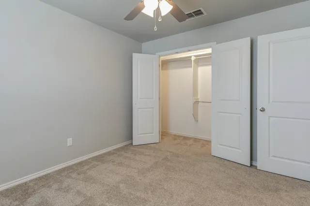 an empty room with a chandelier fan and closet area