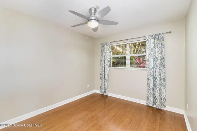 an empty room with wooden floor fan and windows
