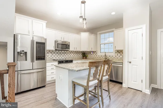 a kitchen with stainless steel appliances granite countertop a refrigerator a sink dishwasher a stove and white cabinets with wooden floor