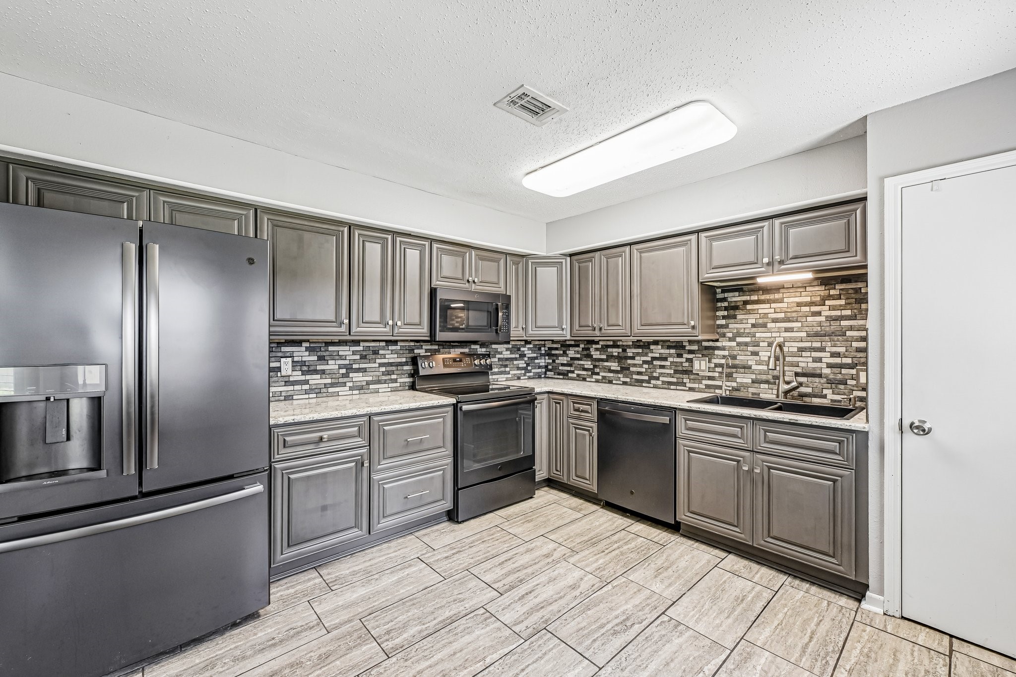 8 Arlington Street Conroe, TX 77301 - Photo 18 of 37 Modern kitchen with sleek gray cabinets, stainless steel appliances, and a stylish tile backsplash. The space features ample storage, a large refrigerator, and a built-in microwave, creating a functional and attractive cooking area.