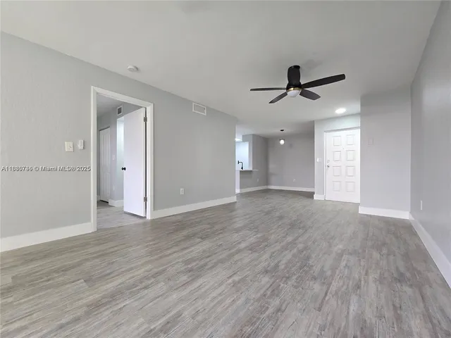 a view of an empty room with wooden floor and a ceiling fan