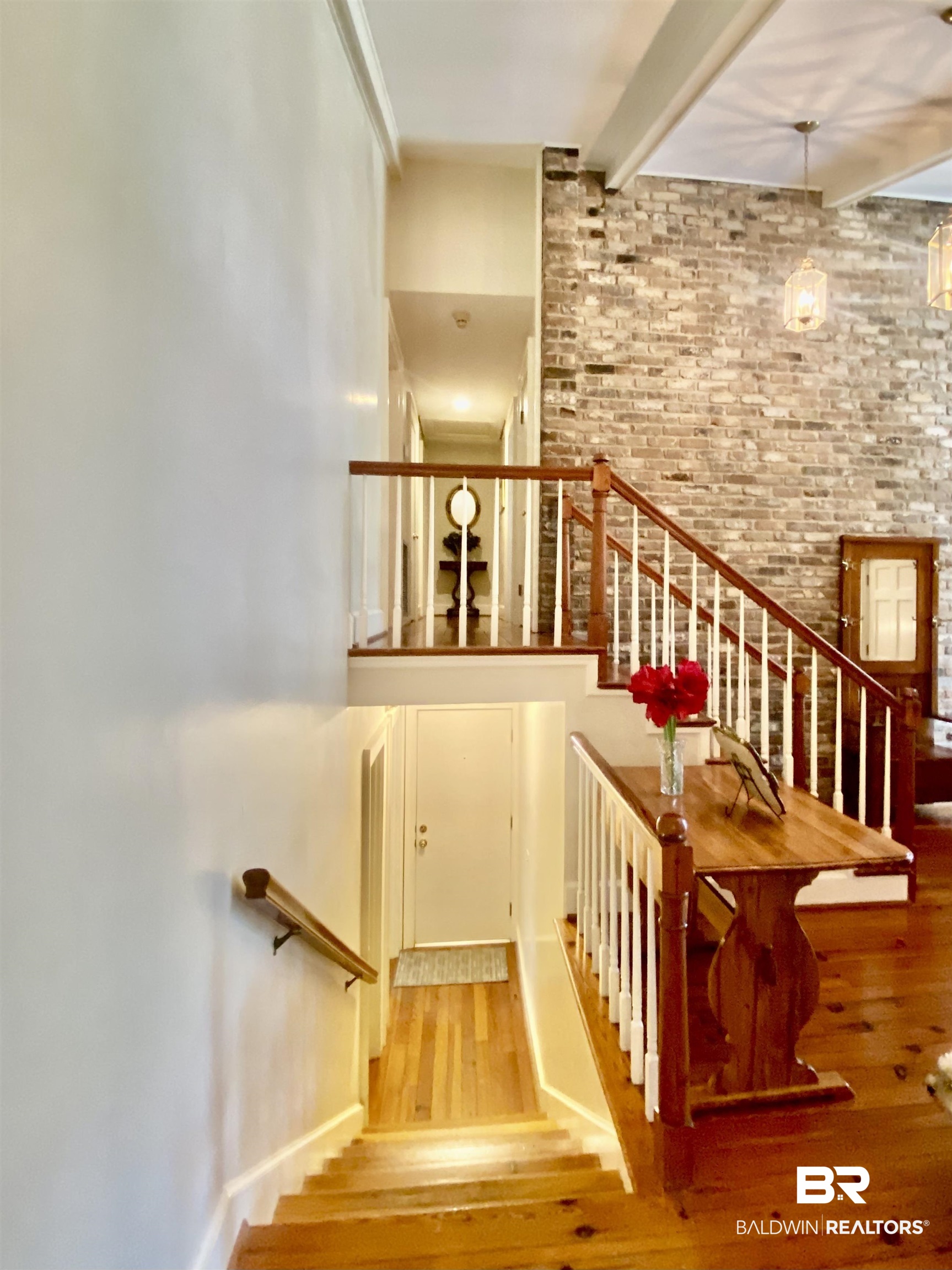 272 Longleaf Circle Monroeville, AL 36460 - Photo 17 of 38 Stairway with brick wall, beamed ceiling, and hardwood / wood-style flooring, leading up to the Primary, Bedrooms 2 & 3. Down leads to carport entrance and Bedroom 4.
