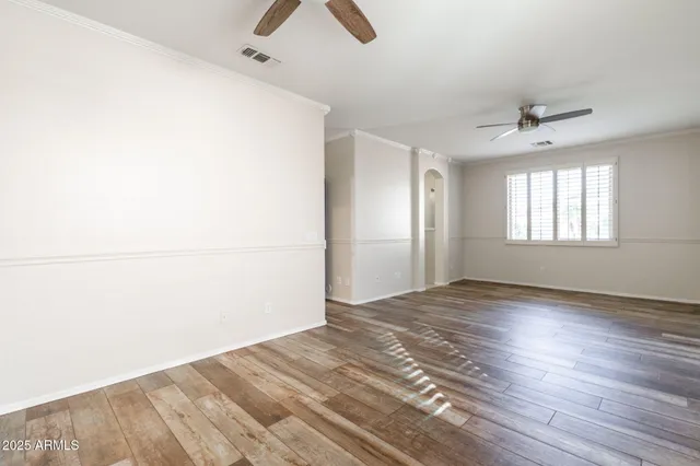 an empty room with wooden floor ceiling fan and windows