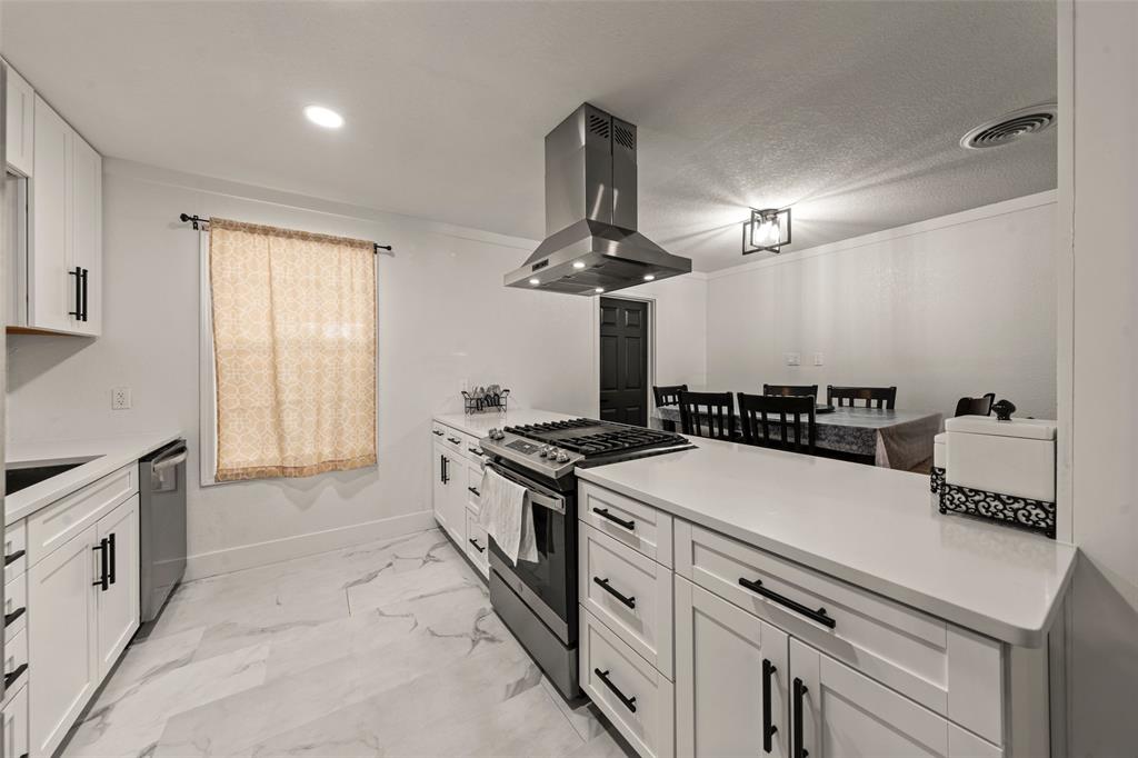 121 Austin Street McGregor, TX 76657 - Photo 8 of 19 Kitchen featuring white cabinets, island exhaust hood, appliances with stainless steel finishes, light marble finish flooring, and a peninsula