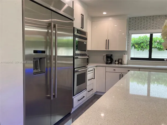 a kitchen with stainless steel appliances kitchen island granite countertop a refrigerator a sink and white cabinets