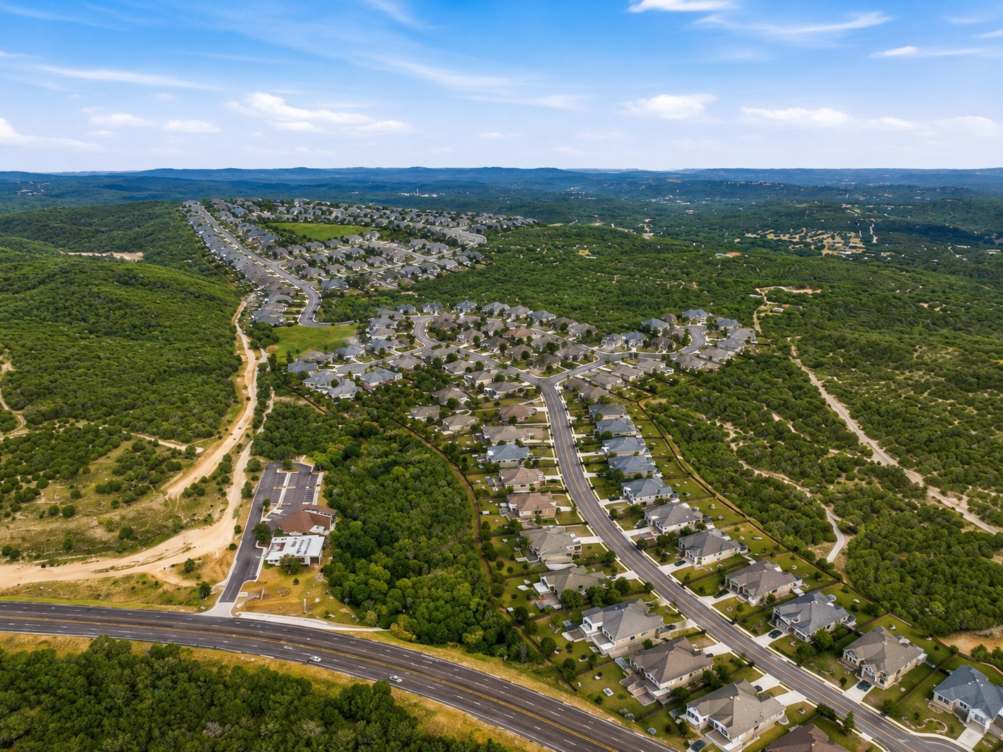 An aerial perspective showcases a quiet residential development nestled among rolling green hills and wooded terrain.