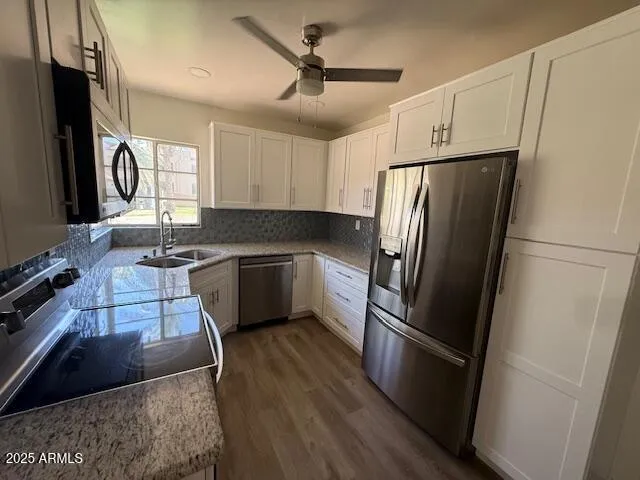 a kitchen with granite countertop a refrigerator a sink a stove and white cabinets