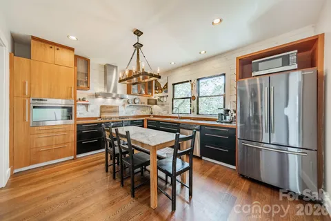 a kitchen with stainless steel appliances granite countertop a refrigerator a stove a sink a dining table and chairs with wooden floor