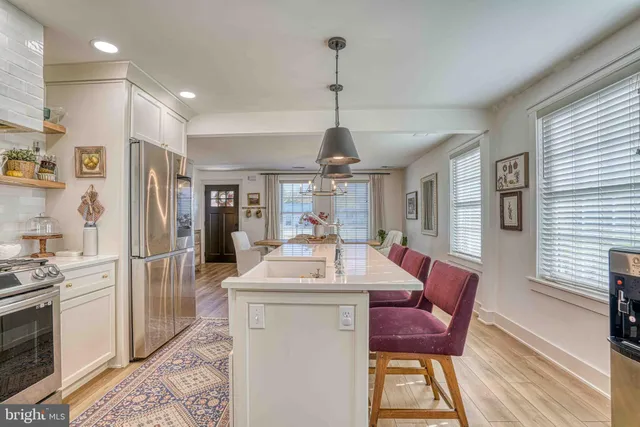 a kitchen with stainless steel appliances kitchen island granite countertop a refrigerator a sink dishwasher a dining table and chairs with wooden floor