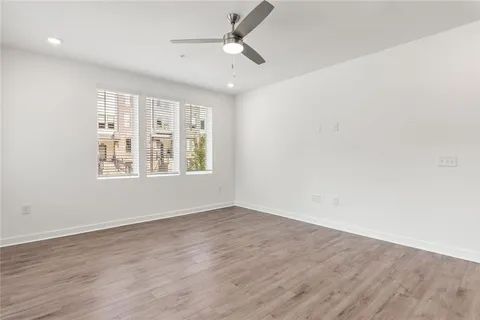 an empty room with wooden floor ceiling fan and windows