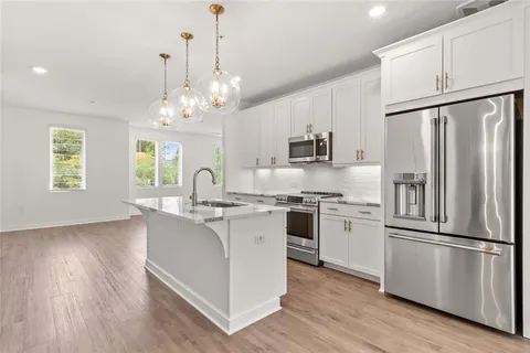 a kitchen with stainless steel appliances granite countertop a refrigerator a stove a sink dishwasher a refrigerator and white cabinets with wooden floor