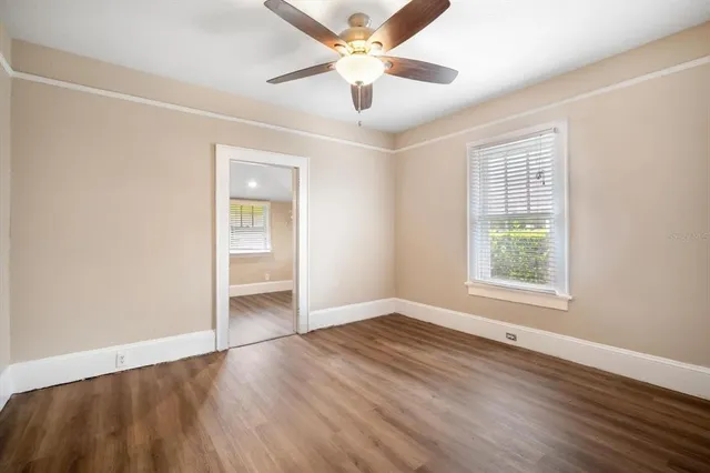 an empty room with wooden floor chandelier fan and windows