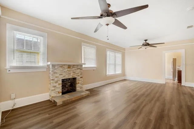 an empty room with wooden floor fireplace and windows