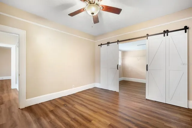 a view of an empty room with wooden floor and a ceiling fan