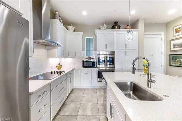 a kitchen with stainless steel appliances kitchen island granite countertop a refrigerator a stove a sink dishwasher and white cabinets with wooden floor