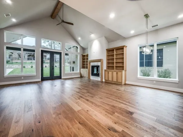 an empty room with wooden floor fireplace and windows