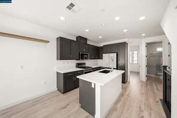 a kitchen with stainless steel appliances a stove top oven a sink a refrigerator white cabinets and wooden floor