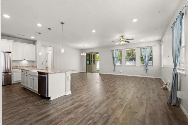 a view of an empty room and kitchen with wooden floor