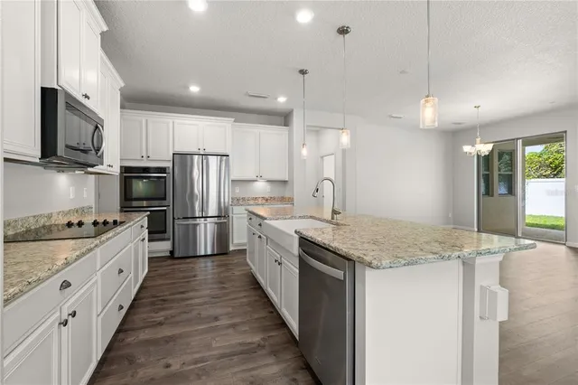 a kitchen with stainless steel appliances kitchen island granite countertop a stove top oven a sink dishwasher a refrigerator and a refrigerator with wooden floor