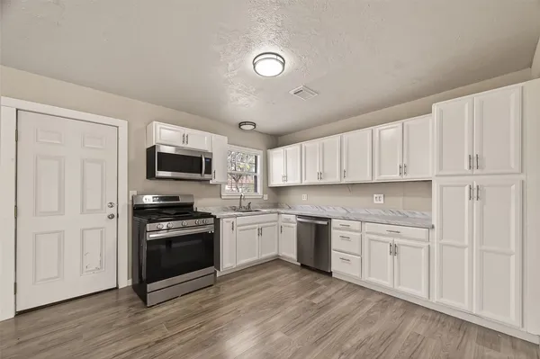 a kitchen with stainless steel appliances granite countertop a stove top oven a sink dishwasher and a refrigerator with wooden floor