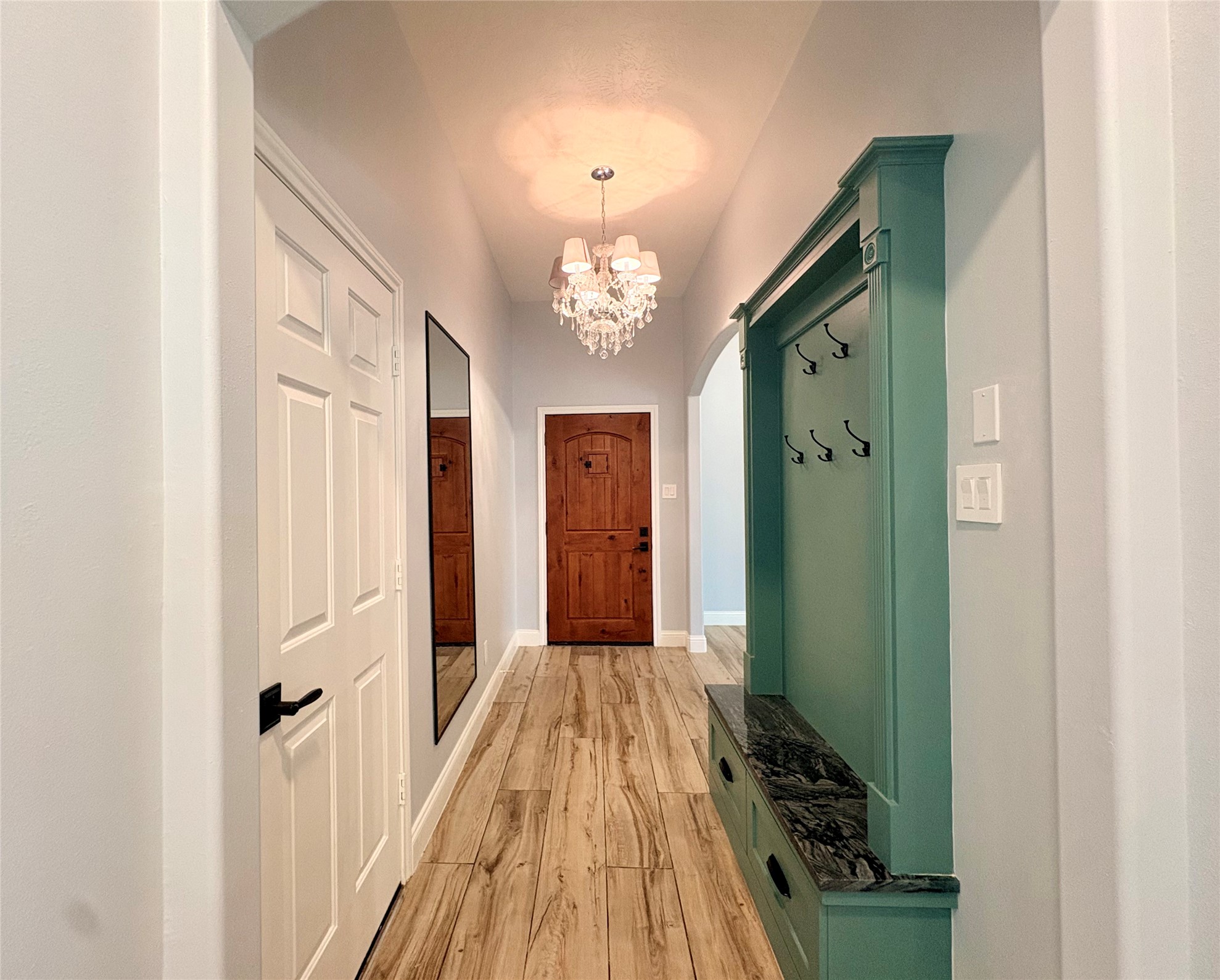 15410 Redbud Berry Way Cypress, TX 77433 - Photo 9 of 49 The entrence features elegant wood flooring, a striking chandelier, and a teal built-in storage bench with hooks. A wooden front door and a large wall mirror add charm and functionality.