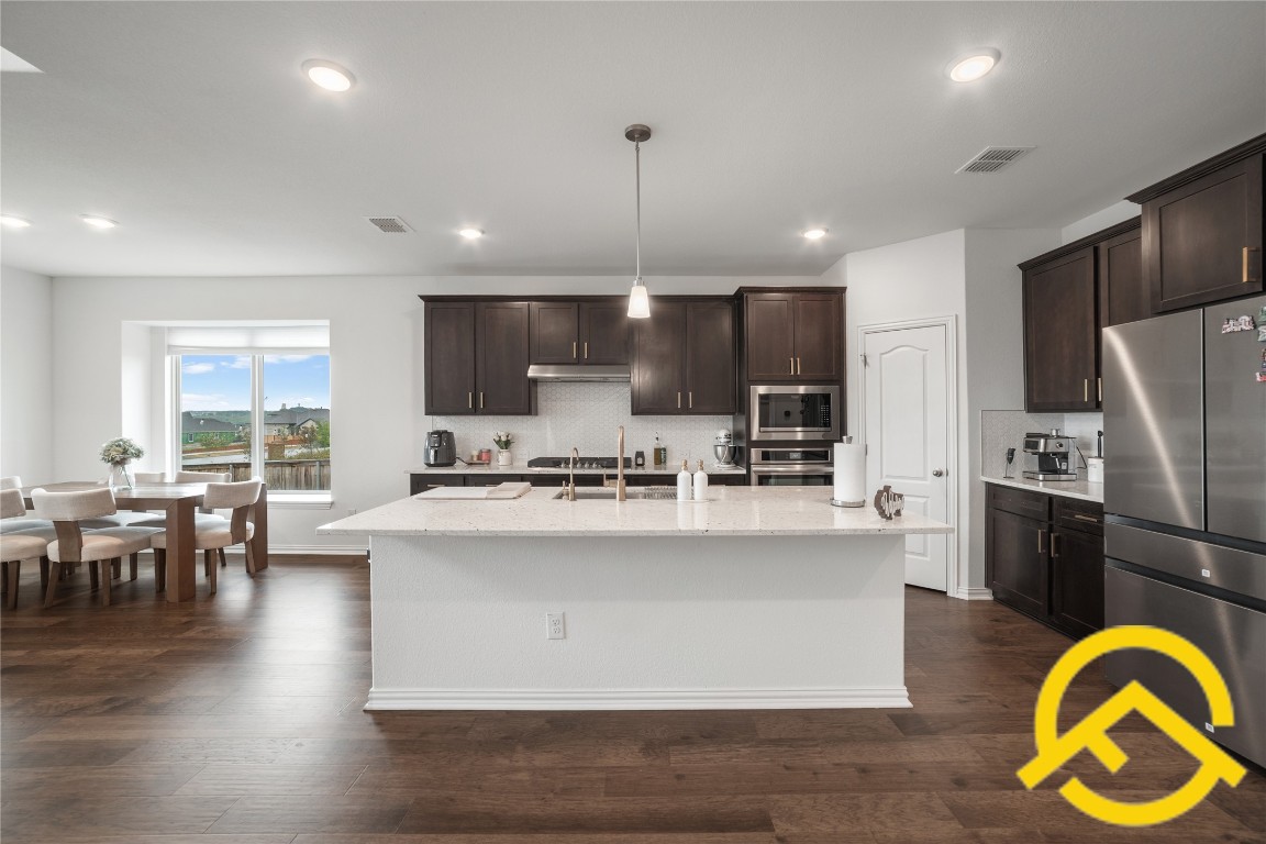 671 Durian Loop Buda, TX 78610 - Photo 5 of 29 a kitchen with kitchen island stainless steel appliances a center island a stove a refrigerator cabinets a dining table and chairs