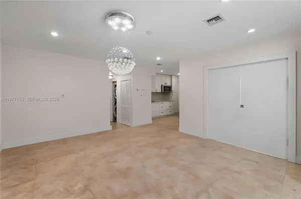 an empty room with a chandelier fan and kitchen view