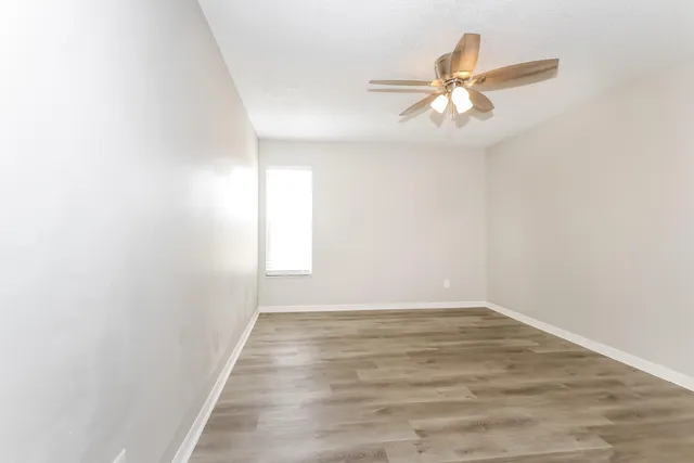 an empty room with wooden floor fan and windows