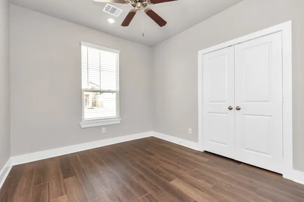 an empty room with wooden floor chandelier fan and windows