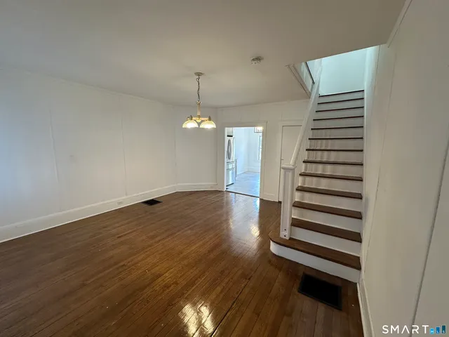 an empty room with wooden floor staircase and windows