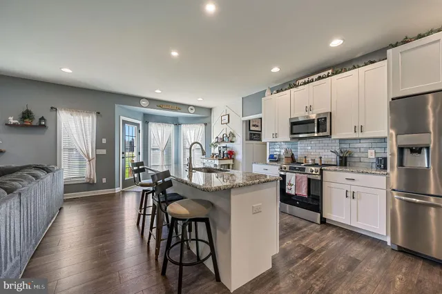 a kitchen with kitchen island granite countertop a stove a sink a refrigerator and white cabinets with wooden floor