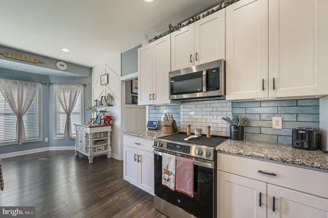 a kitchen with granite countertop a stove top oven a sink dishwasher and white cabinets with wooden floor