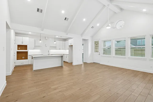 a view of an empty room with kitchen and window