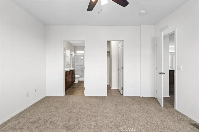 an empty room with chandelier fan and kitchen view
