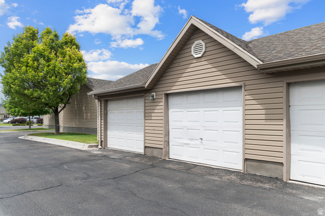 25 West Ridge Road, Unit 25 Saratoga Springs, UT 84045 - Photo 17 of 22 Exterior featuring light brown horizontal siding, a gray shingled roof, white paneled garage doors, and a decorative gable vent